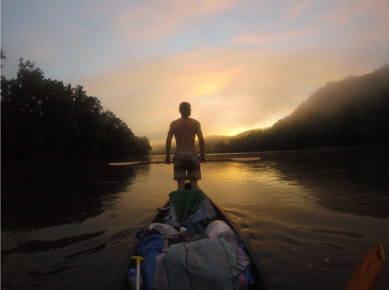 A paddler stands in their boat during sunrise on the river