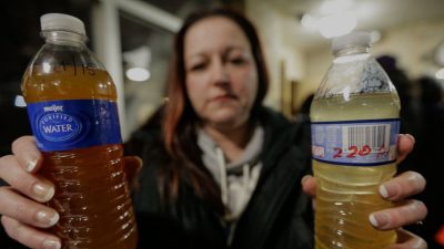 A woman shows two murky water samples in plastic bottles