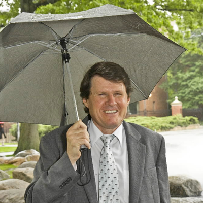 Dr. John Briscoe walking in the rain with an umbrella