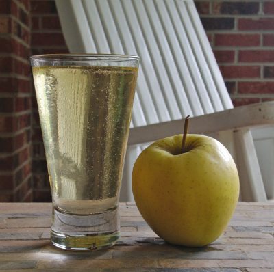 A glass of cider next to an apple